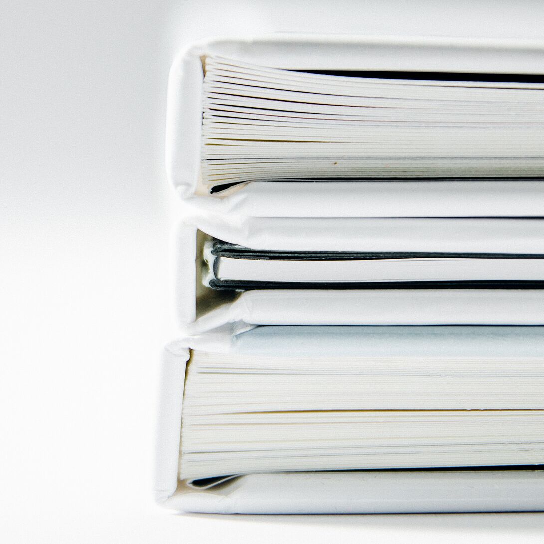 Stacked hardcover books viewed from the side against a light background, partially overlaid with transparent areas of color in shades of green and red.