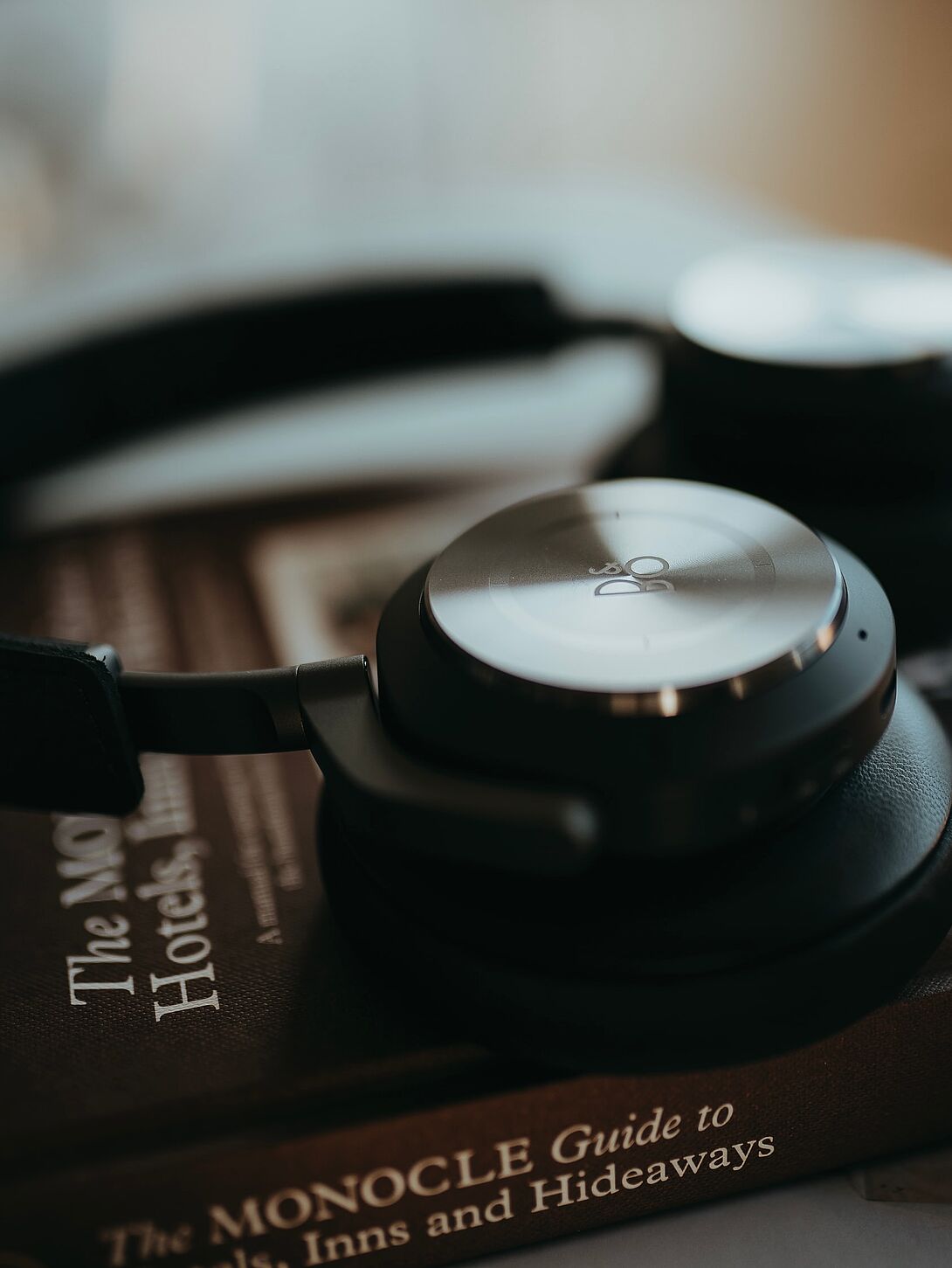 Close-up of over-ear headphones resting on a book, with soft blurring in the background and subtle color overlay.